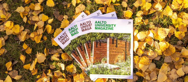 Four Aalto University Magazines on the ground outside, surrounded by yellow autumn leaves. An image of a brown building is on the cover of the magazine.