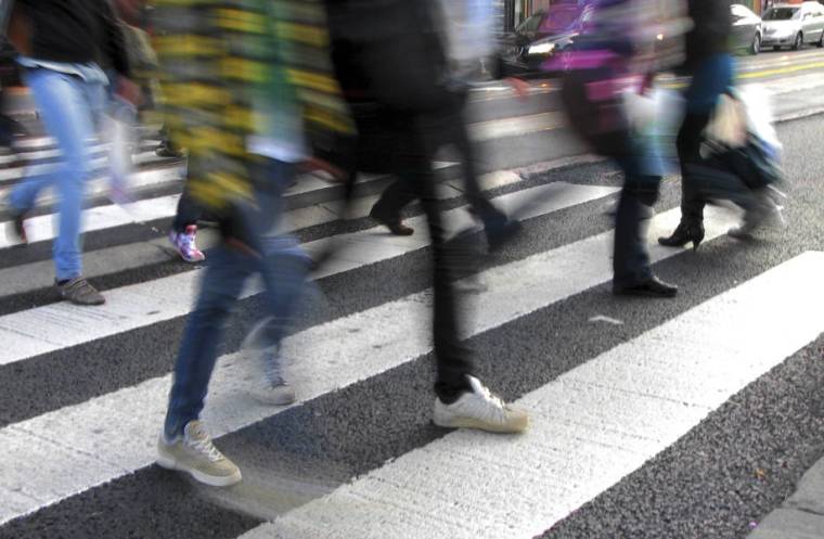 People walking over a road on a zebra crossing. People are wearing blue jeans, sneakers, coats and etc.