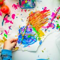 Colorful paint on a table, a child's hand, paintbrushes.