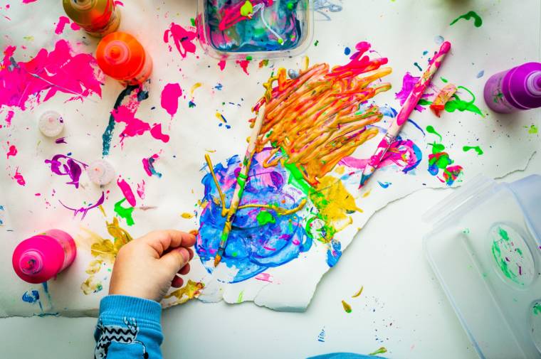 Colorful paint on a table, a child's hand, paintbrushes.