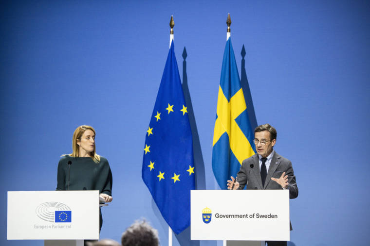 Vasemmalla Euroopan parlamentin presidentti Roberta Metsola ja oikealla ruotsin pääministeri Ulf Kristersson. Keskellä EU:n ja Ruotsin lippu. Sininen tausta.